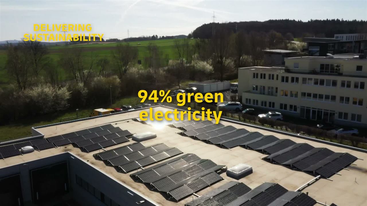 Standbild aus einem Unternehmensfilm: Luftaufnahme eines Firmengebäudes mit Solaranlage auf dem Dach, eingeblendet der Text 94% green electricity